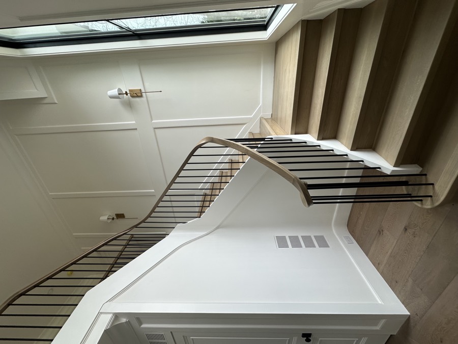 A finished staircase with a curved handrail, panelled walls and light oak treads in a fully renovated home.